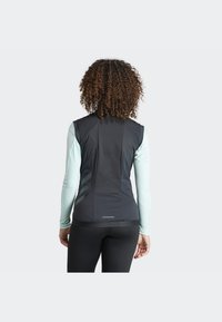 Black vest with a textured back and light blue long sleeves, featuring a sleek design and minimalistic accents.
