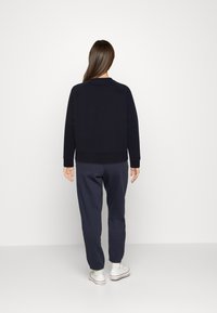 Sudadera navy con cuello redondo y dobladillo acanalado, combinada con pantalones de chándal ajustados a juego y zapatillas blancas. Textura suave.