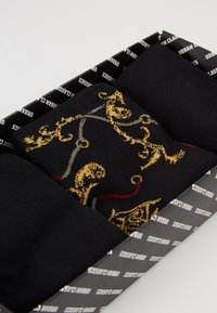 Tre paia di calzini neri in una scatola, con un paio che presenta un motivo ornamentale oro e rosso, materiale di cotone morbido e una consistenza liscia.