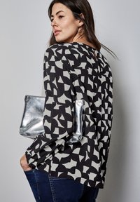 Blusa a righe in bianco e nero con apertura a chiave sul retro, texture morbida, maniche lunghe e una borsa a tracolla metallica argento sotto il braccio.