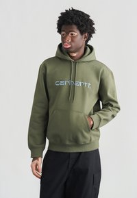 Olivgrüner Hoodie mit einer Fronttasche, einer Kapuze mit Kordelzug und einem hellblauen "carhartt"-Logo. Aus Baumwollmaterial mit weicher Textur.