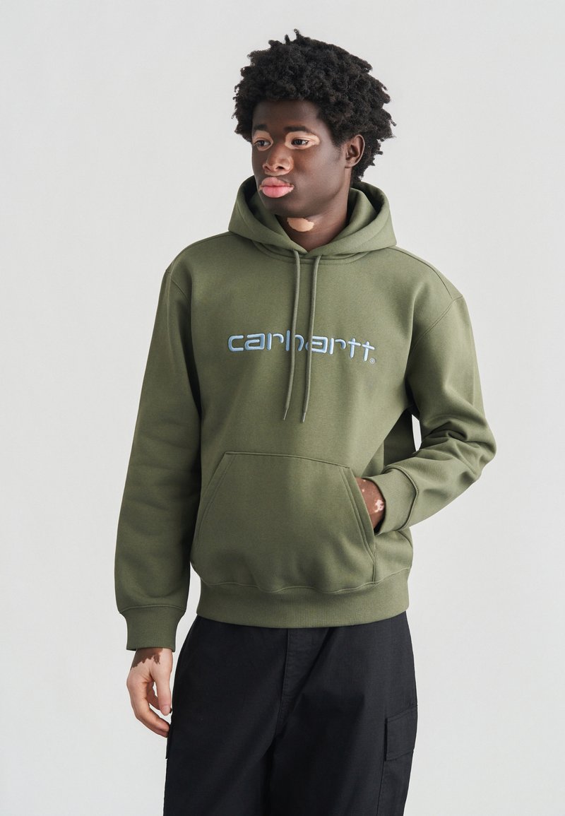 Olivgrüner Hoodie mit einer Fronttasche, einer Kapuze mit Kordelzug und einem hellblauen "carhartt"-Logo. Aus Baumwollmaterial mit weicher Textur.