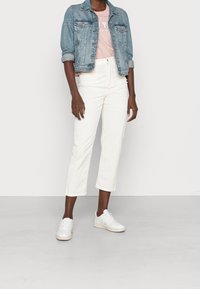 Lysblå denimjakke, sat sammen med en pink grafisk t-shirt og hvide cropped bukser, komplementeret af hvide sneakers.