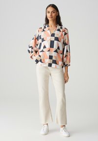 Blusa multicolore con motivi geometrici in pesca, navy e crema, con una vestibilità ampia e scollatura a V. Abbinata a pantaloni flare crema.