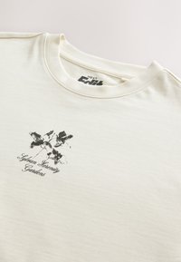 Light cream oversized T-shirt made of cotton; features a black floral print and "Urban Serenity Gardens" text on the front.