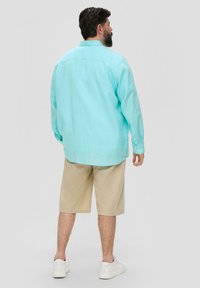 Lichtblauwe linnen blouse met lange mouwen en knoopmanchetten, gecombineerd met beige shorts en witte sneakers, gezien van achteren.