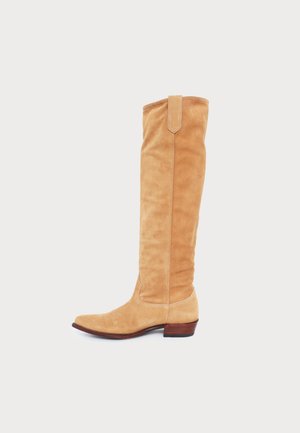 Botte en daim fauve montant jusqu’au genou, à bout pointu, petit talon contrecollé et languette de tirage, présentée de profil.