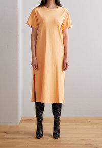 Pomarańczowa sukienka midi z krótkim rękawem wykonana z miękkiej bawełny, z bocznymi rozcięciami. Połączona z czarnymi, wysokimi do kolan botkami z tłoczonego wąż skóry.