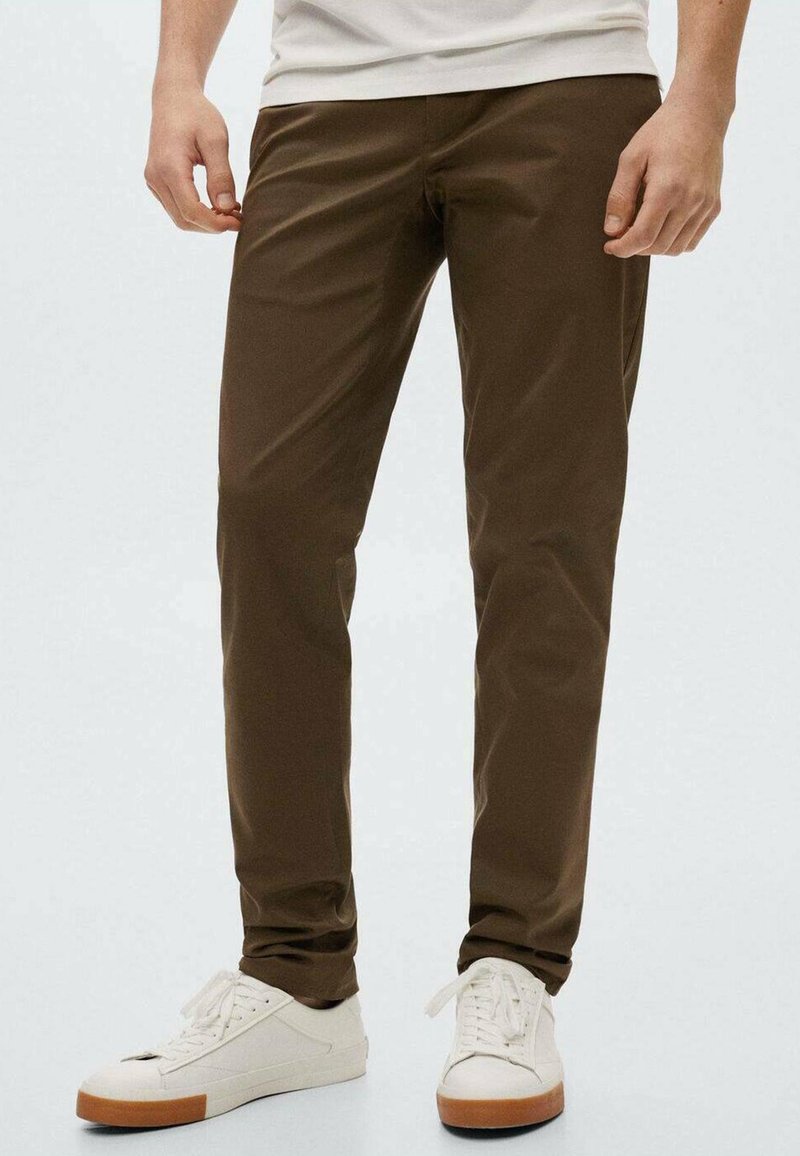 Hnědé slim-fit kalhoty vyrobené z lehkého materiálu, s hladkou texturou a strukturovaným designem, doplněné bílými teniskami.