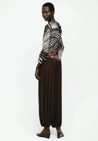 Blusa con stampa zebrate in bianco e nero con maniche lunghe, abbinata a pantaloni a pieghe marroni. Tessuto dalla trama liscia, completato da scarpe nere con zeppa.