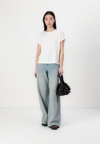 T-shirt bianco in cotone con maniche corte, abbinata a jeans a pieghe azzurri chiari. Porta una borsa nera con motivo floreale. Design semplice.