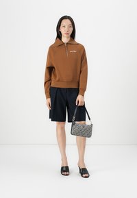 Brown zip-up sweatshirt with comfortable fit, navy shorts, black slide sandals, and a patterned shoulder bag featuring a clasp and strap.
