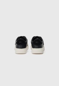 Sneaker in pelle nera con suola bianca, caratterizzati da una finitura liscia e un colletto imbottito. Logo impresso sul retro.