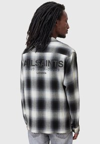 Camisa de franela a cuadros en blanco y negro con un ajuste relajado, mangas largas y el logo "ALLSAINTS" impreso en la parte posterior.