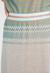 Vævet kjole med et zigzag-mønster i teal, orange og hvid, med en kontrasterende hvid talje og en tekstureret overflade.