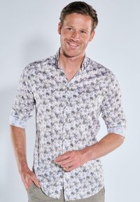 Hemd aus leichtem Stoff mit weißem Hintergrund und floralem Muster in Grün und Grau. Hochgerollte Ärmel zeigen einen kontrastierenden Manschette.