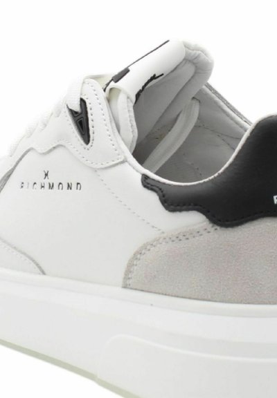 Sneaker bianca realizzata in pelle e suede, con un accentuato tallone nero, logo impresso e una suola spessa bianca.