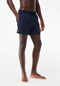 Marineblaue Badeshorts aus leichtem Stoff, mit einem Kordelzugbund, Seitentaschen und einem kleinen grünen Logo am Saum.