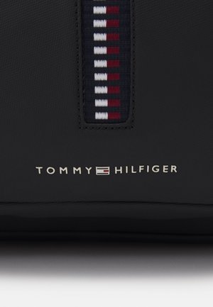 Schwarze Lederoberfläche mit einem angenähten Stoffstreifen in Rot, Weiß und Marineblau sowie dem Markennamen "Tommy Hilfiger" in weißen Buchstaben darunter.