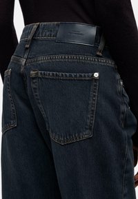 Donkere denim jeans met een hoge taille, met opvallende achterzakken en contrasterende stiksels. De tailleband heeft een leren merkembleem.