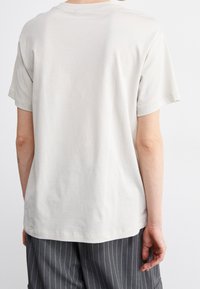 Svetle béžové bavlněné tričko s volným střihem, krátkými rukávy a kulatým výstřihem, s hladkým texturem a bez viditelných vzorů.