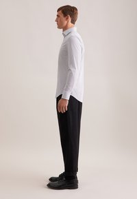 Witte lange mouw shirt met een klein blauw patroon, gecombineerd met zwarte broeken en zwarte schoenen. Het shirt heeft een standaard kraag en knoopdetails.
