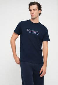 Marineblauwe katoenen t-shirt met korte mouwen, met een kleurrijk "tommy JEANS" logo over de borst in een vet gedrukt lettertype.