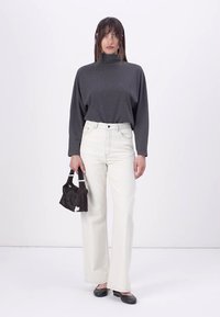 Grå turtleneck, hvite høy midje vide jeans og svarte leiligheter. En liten svart håndveske med hvit aksent holdes i venstre hånd.