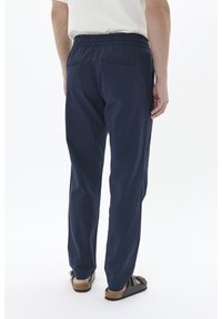 Pantalones de tela ligera en azul marino con cinturilla elástica, que cuentan con dos bolsillos traseros y un diseño de pierna recta. Combinados con sandalias marrones.