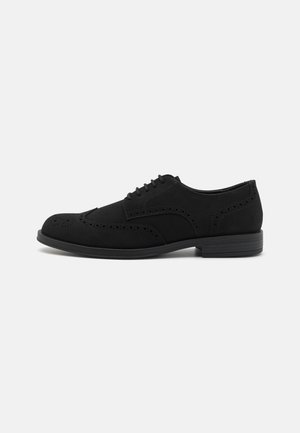 Schwarze Wildlederschuhe im Oxford-Stil mit dekorativen Perforationen, runder Zehenpartie und niedriger, gestapelter Sohle. Standard-Lace-Up-Design mit sechs Ösen.