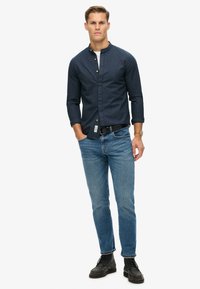 Donkerblauwe overhemd met rechte kraag, gecombineerd met lichtblauwe jeans en zwarte veterschoenen. Heeft een casual ontwerp en pasvorm.