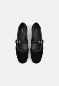Scarpe Mary Jane in velluto nero con suola piatta, punta arrotondata e cinturino regolabile. Fodera interna liscia e design minimalista.