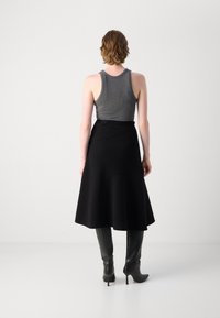 Black flared skirt made of textured fabric, featuring an asymmetrical design. Paired with a gray tank top and black knee-high boots.