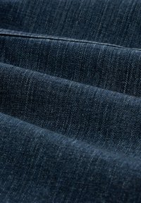 Sötétkék farmeranyag, finom textúrával és változó �árnyalatokkal. Az anyag szoros szövést mutat, amelyen halvány átlós vonalak láthatók.