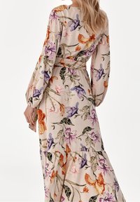 Blomstermaxikjole i lys beige stof med lilla, orange og pink blomster. Lange ærmer, indsnævret talje og lagdelt kantdesign.