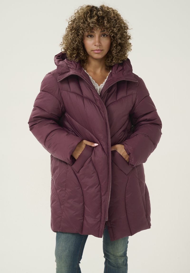 Burgundska puffer jakna z zadrgo spredaj, kapuco in diagonalnim quiltanjem. Ima stranske žepke in udoben kroj. Nosi se čez čipkast zgornji del.