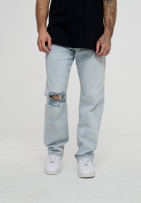 Lys blå ripped jeans med merkbare, frynsete detaljer ved kneet, parret med en svart t-skjorte og hvite sneakers. Laget av bomulls materiale.