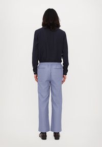 Blaue, locker sitzende Hose mit einem elastischen Bund, kombiniert mit einem dunklen Langarmshirt; einfarbige Textur, keine sichtbaren Muster oder Akzente.