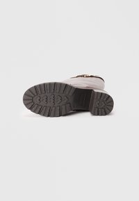 Bottine en cuir brun avec une épaisse semelle en caoutchouc noir, présentant un relief texturé pour une bonne adhérence et un détail de boucle en or ornée.