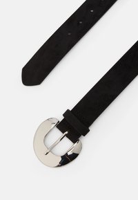 Curea din suede negru, cu o cataramă mare din metal argintiu, având o textură netedă și mai multe găuri de ajustare pentru mărime.
