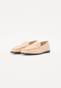 Beige læder loafers med en forhøjet søm, blød tekstur og en lav hæl. Har et lille præget logo på den øverste side.