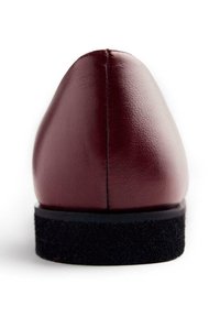 Vue arrière d'une chaussure habillée en cuir rouge foncé avec une semelle noire texturée sur un fond blanc.