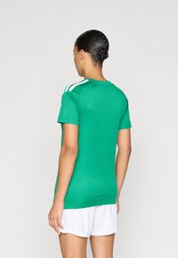 Πράσινη αθλητική φανέλα με κοντά μανίκια, στρογγυλή λαιμόκοψη και λευκές κάθετες ρίγες στους ώμους. Λείο ύφασμα και εφαρμοστή γραμμή.