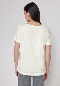 Lys cream kortærmet t-shirt, blød tekstur, rund halsudskæring, afslappet pasform, med matchende jeans og minimalistiske sølvøreringe.