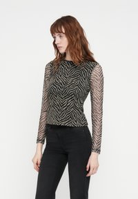 Sheer long-sleeve top with a black and beige zebra stripe pattern, round neckline, and fitted silhouette. Worn with black pants.