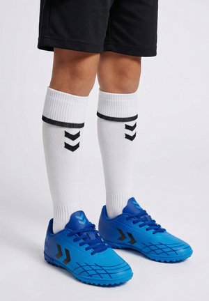 Dziecko noszące białe sportowe skarpetki do kolan z czarnymi pasami w kształcie litery V oraz niebieskie buty piłkarskie z czarnymi detalami na białym tle.