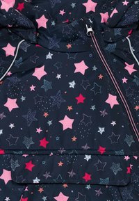 Veste marine avec un motif d'étoiles sur l'ensemble en rose, blanc et bleu, avec une fermeture éclair et une capuche, fabriquée à partir d'un matériau lisse et léger.