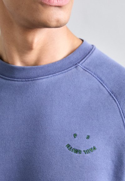 Lys lilla sweatshirt med ribbet halslinning og et grønt brodert smilende ansikt med teksten "PAUL SMITH." Glatt bomullsblandingsstoff.
