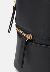 Black textured handbag featuring a gold zipper and accent detailing. The bag has a smooth finish with a side zipper pocket.