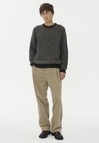 Masivni pleteni pulover v temno modri barvi z večbarvnimi madeži, rebrastimi manšetami, v kombinaciji s bež kord skirt hlačami in črnimi čevlji z rdečimi vezalkami.